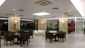 A modern hotel lobby with a marble staircase, a seating area with tables and chairs, and a stone accent wall. - Antonios Village (Pineios)