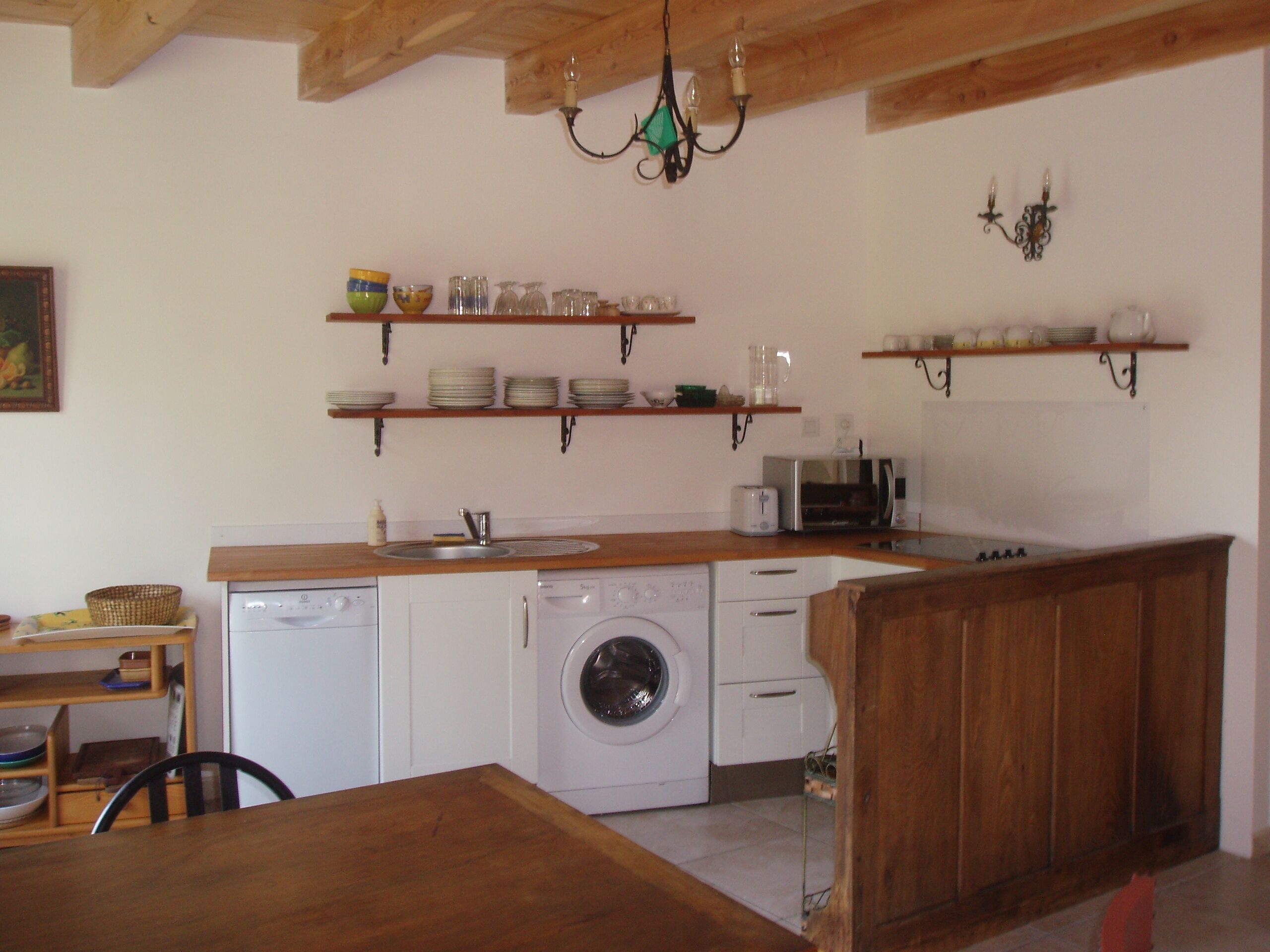 A compact kitchen with wooden countertops, a washing machine, and a dining area with a table and chairs.