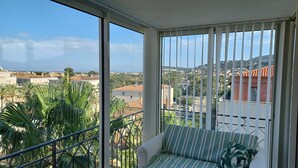 Ein Balkon mit einer Sitzecke und Metallgeländer, mit Blick auf eine Wohngegend mit Häusern und Palmen.