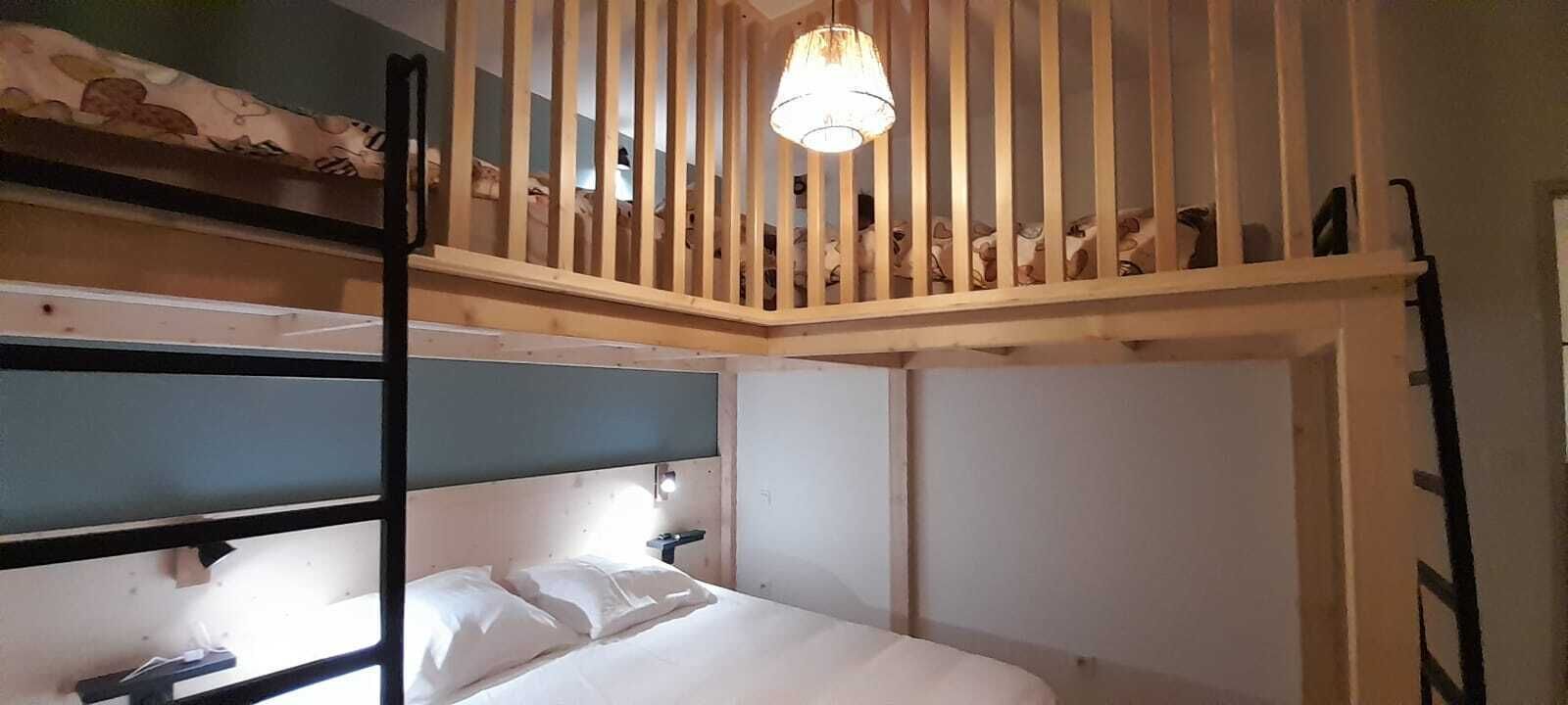Une chambre avec un lit superposé, un plafond avec des lattes en bois, un lit simple avec une literie blanche et un luminaire fixé au mur.