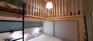 A bunk bed room with a wooden slat ceiling, a single bed with white bedding, and a wall-mounted light fixture.