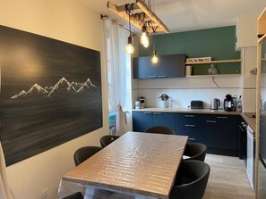 A modern kitchen with dark cabinets, a wooden table, and a mountain painting on the wall.