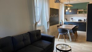 Un salon moderne avec un canapé foncé, une table basse en verre et un coin repas comprenant une table et des chaises en bois.