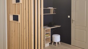 Une pièce avec une cloison en bois, un bureau avec un ordinateur, des étagères et un petit tabouret.