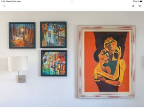 A wall with four framed paintings and a lamp.