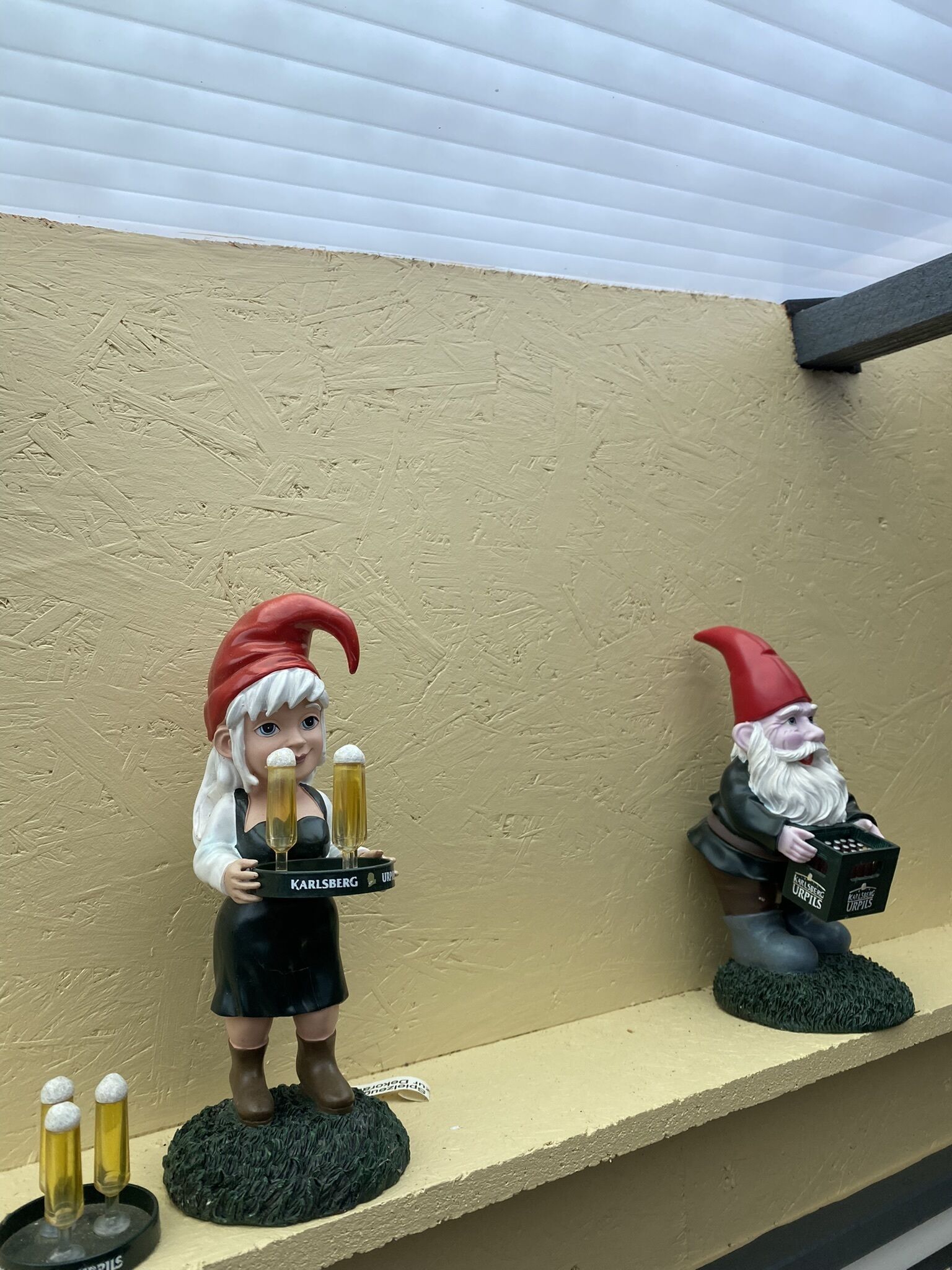 Dos figuritas de gnomos sobre una estantería frente a una pared con textura.