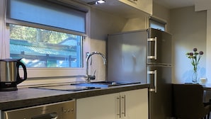 Une cuisine moderne équipée d’un lave-vaisselle, d’appareils électroménagers en acier inoxydable et d’une fenêtre donnant sur un bâtiment traditionnel.