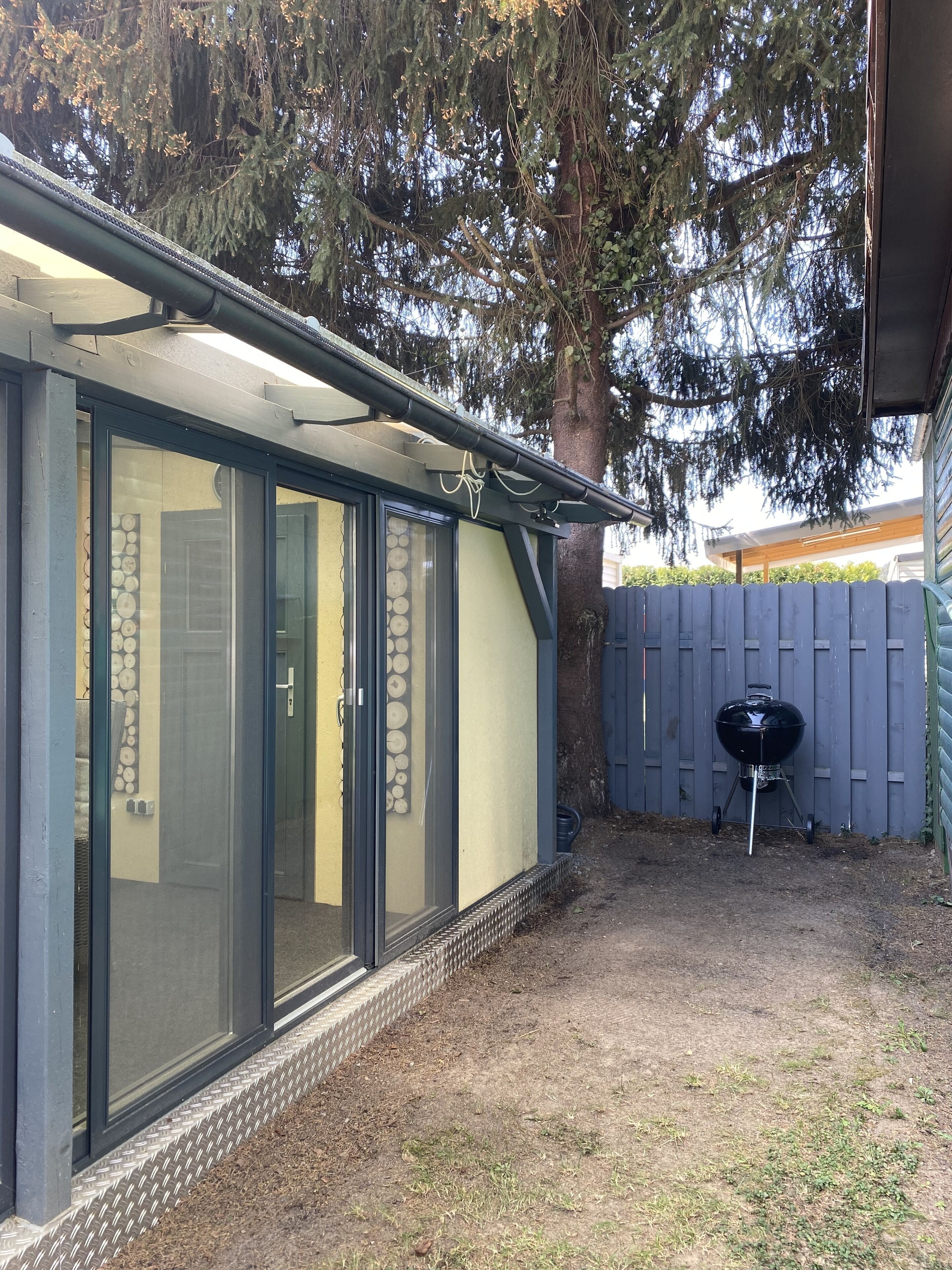 Une terrasse couverte avec des portes-fenêtres coulissantes, un barbecue et une clôture en bois.