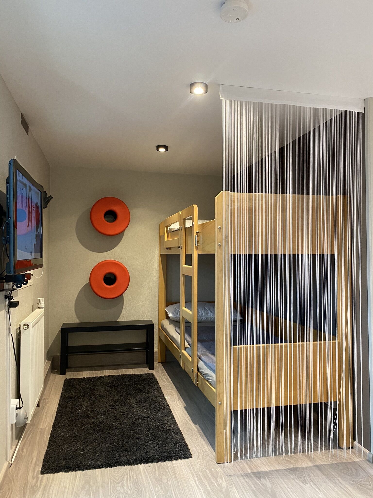 Una habitación con literas, alfombra negra, un banco y dos decoraciones circulares naranjas en la pared.