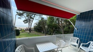 Ein Balkon mit rotem Markisenstoff, weißen Plastikstühlen und einem weißen Tisch.