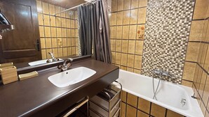 A bathroom with a wooden vanity, a large mirror, a bathtub, and tiled walls. - Studio at Les Gets ski lift, modern comfort (Les Gets)