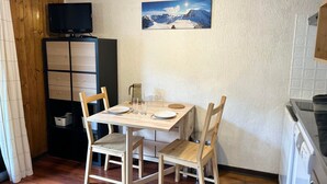 A small dining area with a wooden table, two chairs, a television, and a painting on the wall. - Studio at Les Gets ski lift, modern comfort (Les Gets)