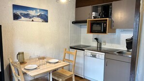 A compact kitchen with a dining area, including a wooden table, chairs, a microwave, a dishwasher, and a small cabinet. - Studio at Les Gets ski lift, modern comfort (Les Gets)