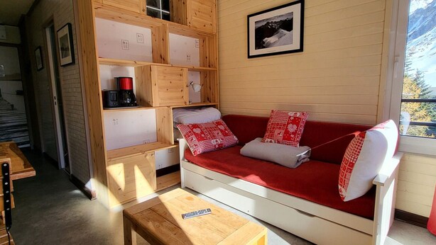 Ein gemütliches Zimmer mit einer Holzsofa, einem kleinen Holztisch und integrierten Regalen.