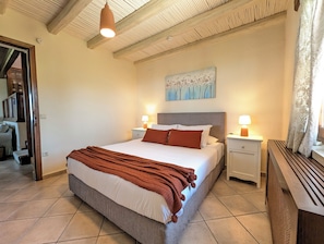 A bedroom with a bed, nightstands, a painting, and a window with curtains.