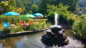 Ein Garten mit Teich, Springbrunnen und Gartenmöbeln mit Sonnenschirmen.
