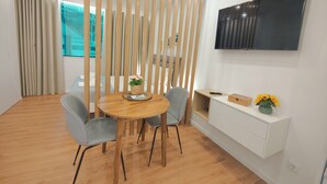 Un espace repas moderne avec une table ronde en bois, des chaises à revêtement gris, un panier tressé rempli de fleurs et un meuble console blanc orné d’un vase de tournesols.