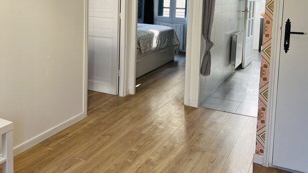 A hallway with wooden flooring, a bed with a patterned bedspread, a radiator, and a door with a patterned wall. - Appart PARIS Sud★ calm & bright - RER B 2 minutes (Cachan)