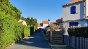 A narrow residential street lined with houses, a wooden fence, and dense greenery. - Comfortable Cottage 4 Pers, Beach 200m, Private Parking (La Faute-sur-Mer)