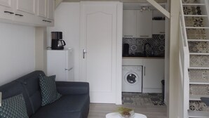 A compact living space with a sofa, a coffee machine, a washing machine, and a staircase with patterned tiles. - Comfortable Cottage 4 Pers, Beach 200m, Private Parking (La Faute-sur-Mer)