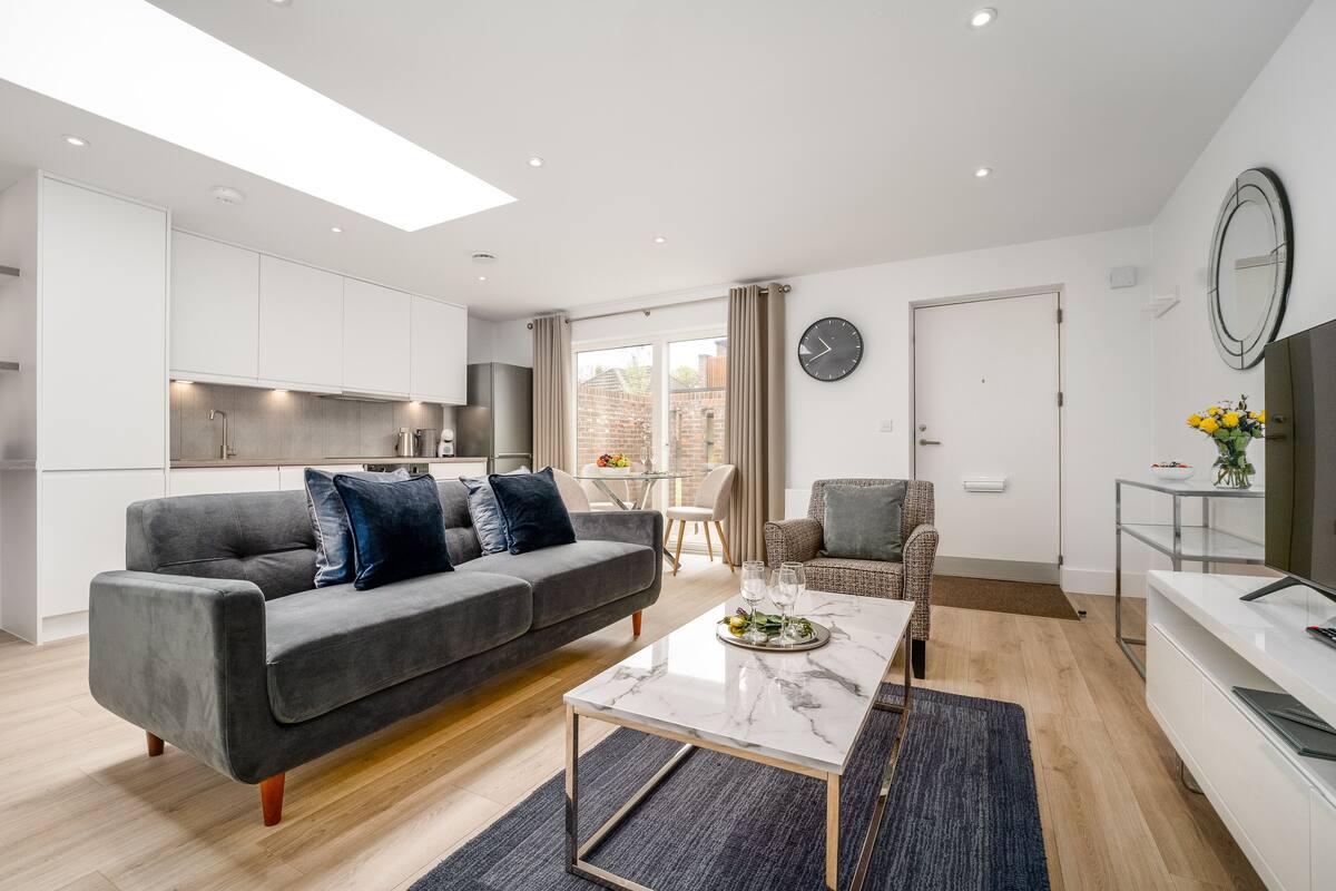 Un salon moderne avec un canapé gris, une table basse en marbre et un téléviseur posé sur un meuble blanc.