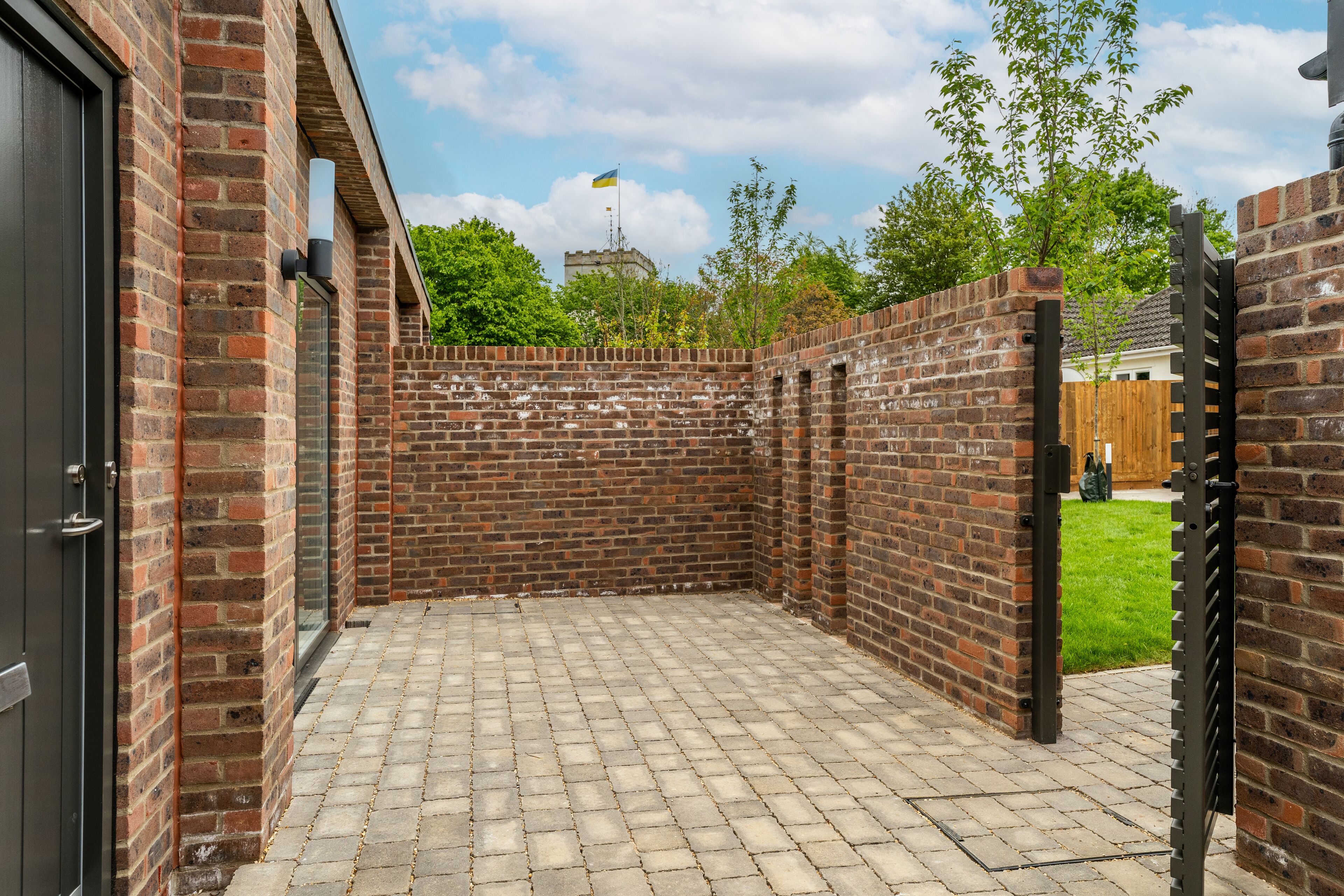 A brick wall with a flag, a paved patio, and a wooden gate.