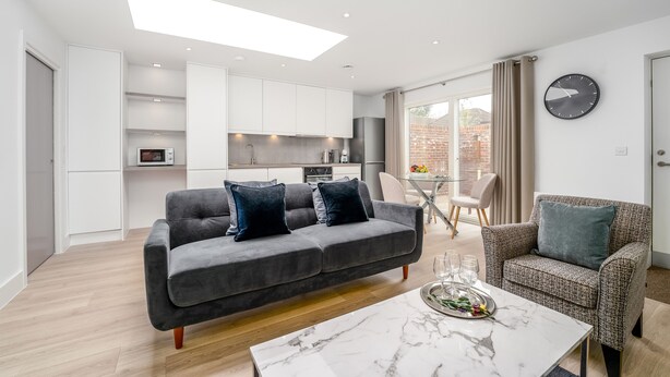 Ein modernes Wohnzimmer mit grauem Sofa, einem gemusterten Sessel und einem Marmortisch.