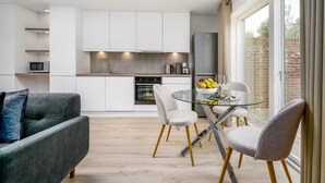 Eine moderne Küche mit weißen Schränken, ein Essbereich mit einem Glastisch und ein graues Sofa.