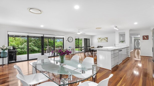 A modern kitchen with a central island, large windows, and a dining area with a glass table and chairs.