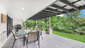 An outdoor patio with a glass table and chairs, a grill, and a covered area with a view of a garden. - PARKSIDE - THE VINTAGE HOLIDAY HOUSES (POKOLBIN)
