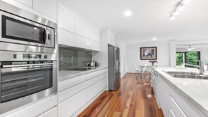 A modern kitchen with stainless steel appliances, white cabinetry, and a wooden floor.
