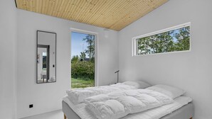 A modern bedroom with a large bed, two windows, and a wooden ceiling. - Beach front home in Haderslev (Haderslev)