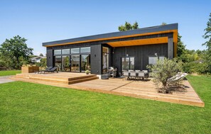 Una casa moderna con terraza de madera, ventanas grandes y mobiliario exterior.
