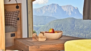 Ein gemütliches Zimmer mit einem Holztisch, einer Schüssel Äpfel, einer herzförmigen Aussparung und Blick auf Berge.