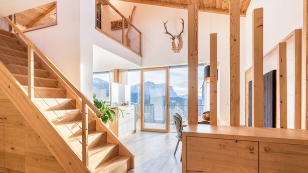 Eine Holztreppe führt zu einem Balkon mit Bergblick, einem Holztisch und einer Dekoration aus Hirschgeweih.