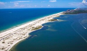 Vista aérea de una zona costera con una extensa playa de arena, un océano azul cristalino y un pequeño asentamiento con edificios cerca de la orilla.