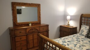 Un dormitorio con un aparador de madera, una mesita de noche con lámpara y una cama con colcha estampada.