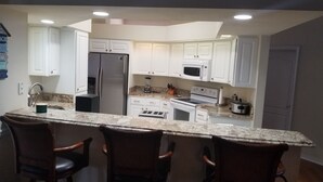 A kitchen with white cabinets, a stainless steel refrigerator, a microwave, a stove, and a toaster. There are three wooden chairs at the counter. - Exclusive 2850 sf Pool Home near Perdido Beaches & NAS, Heated Pool, 2 Masters! (Pensacola)