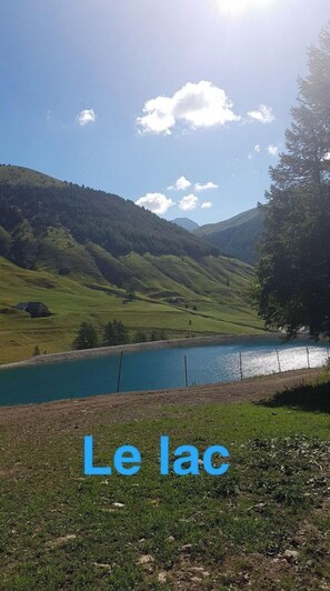 Vista panorâmica do Le Lac, com céu claro, colinas verdes e um lago.