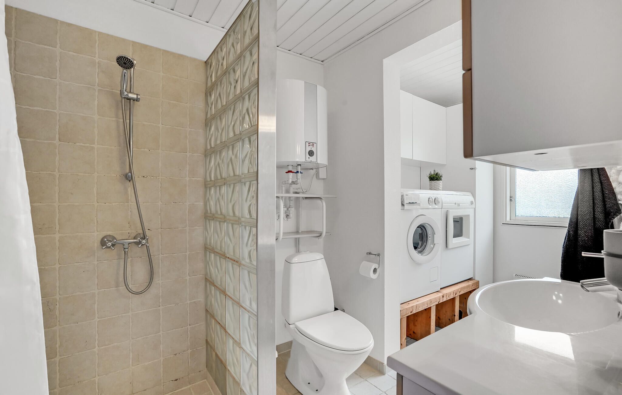 Et moderne badeværelse med brusebad, toilet, vaskemaskine og håndvask.