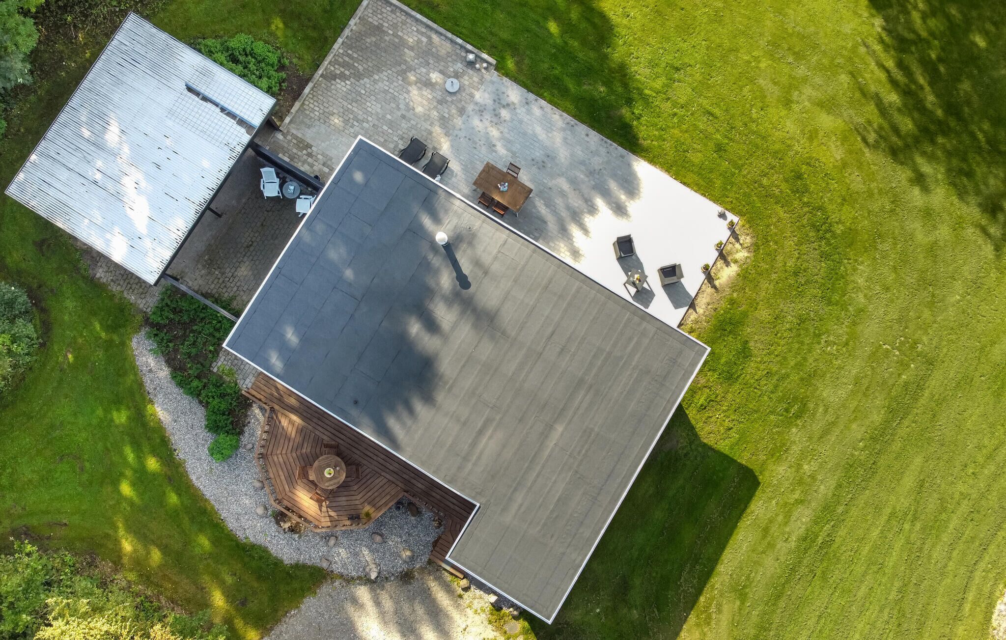 Luchtbeeld van een modern huis met een plat dak, een terras met tuinmeubilair en een verzorgd gazon.