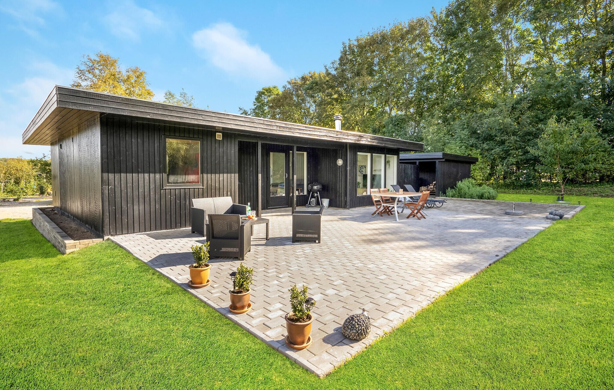 Ein modernes Haus mit einer Terrasse, Gartenmöbeln und Topfpflanzen.