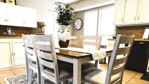 A dining area with a wooden table and chairs, a vase with flowers, and a clock on the wall.