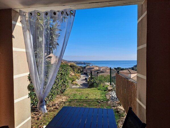 A balcony with a view of the sea, a garden, and a pathway leading to houses.