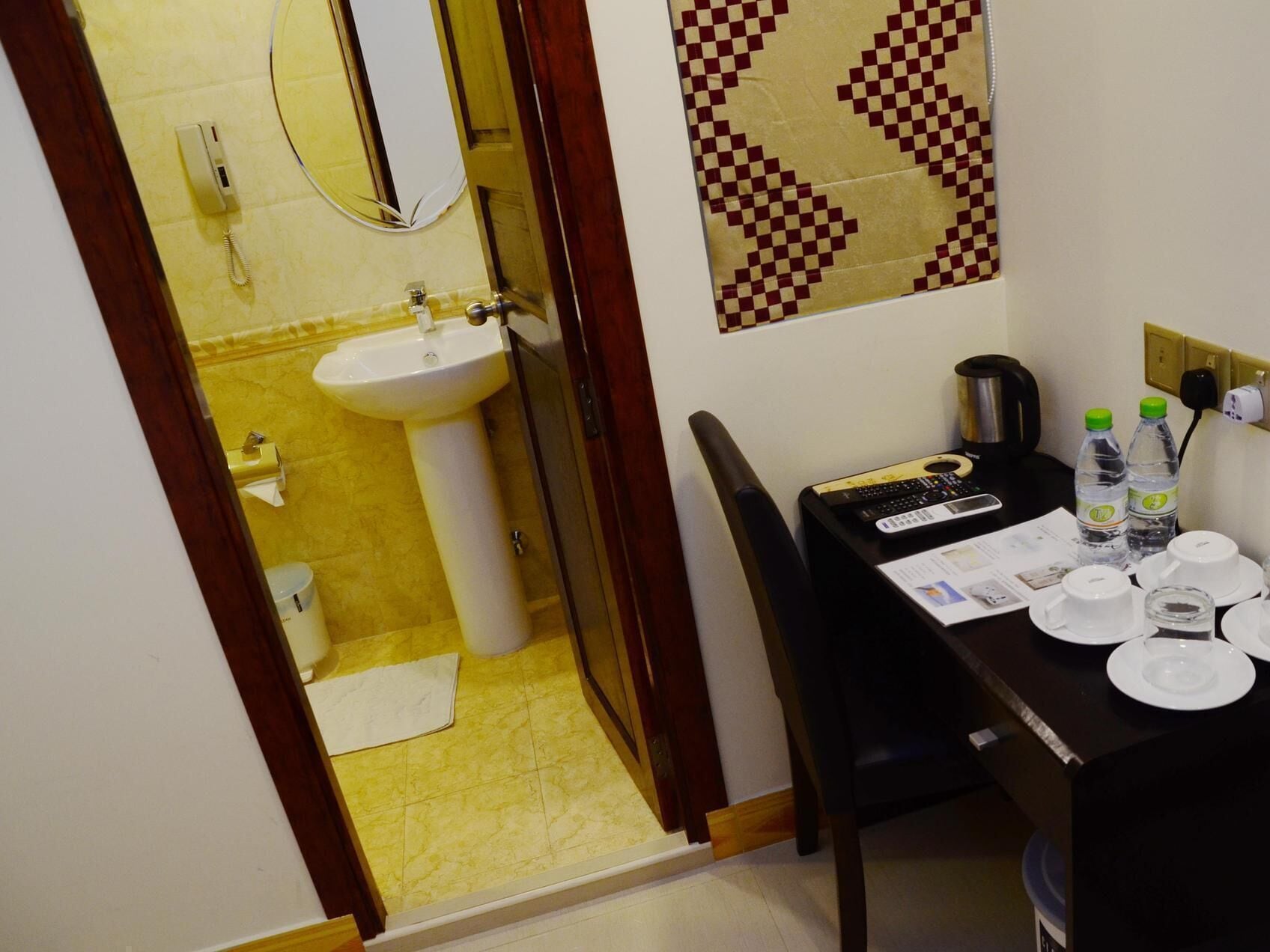 Una habitación de hotel con baño, un comedor con una mesa para dos personas y una cafetera.