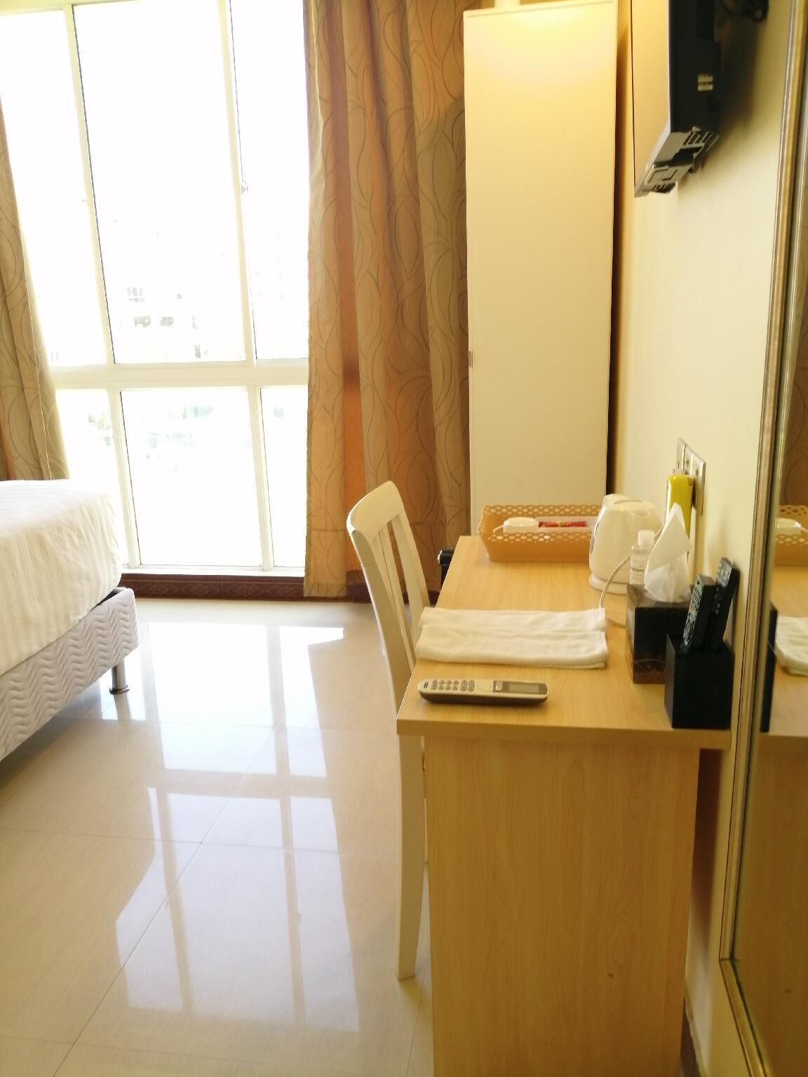 A hotel room with a bed, a desk with a chair, a remote control, and a telephone.