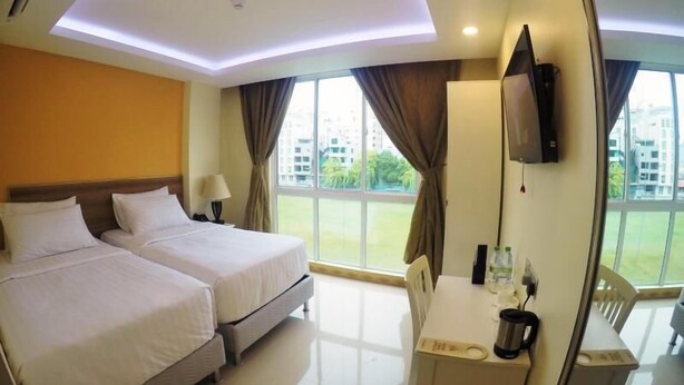 A hotel room with two beds, a dining table, a TV, and large windows with curtains. - The Grand View (Malé)