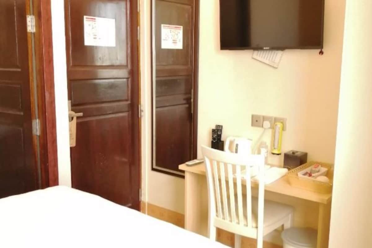 Habitación de hotel con cama, escritorio con silla, televisor y un pequeño cubo de basura.
