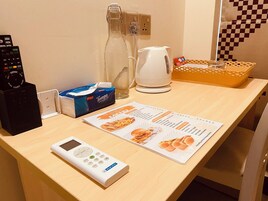 Habitación de hotel con un escritorio de madera, un reloj digital, una caja de pañuelos, un menú, una tetera y un control remoto.