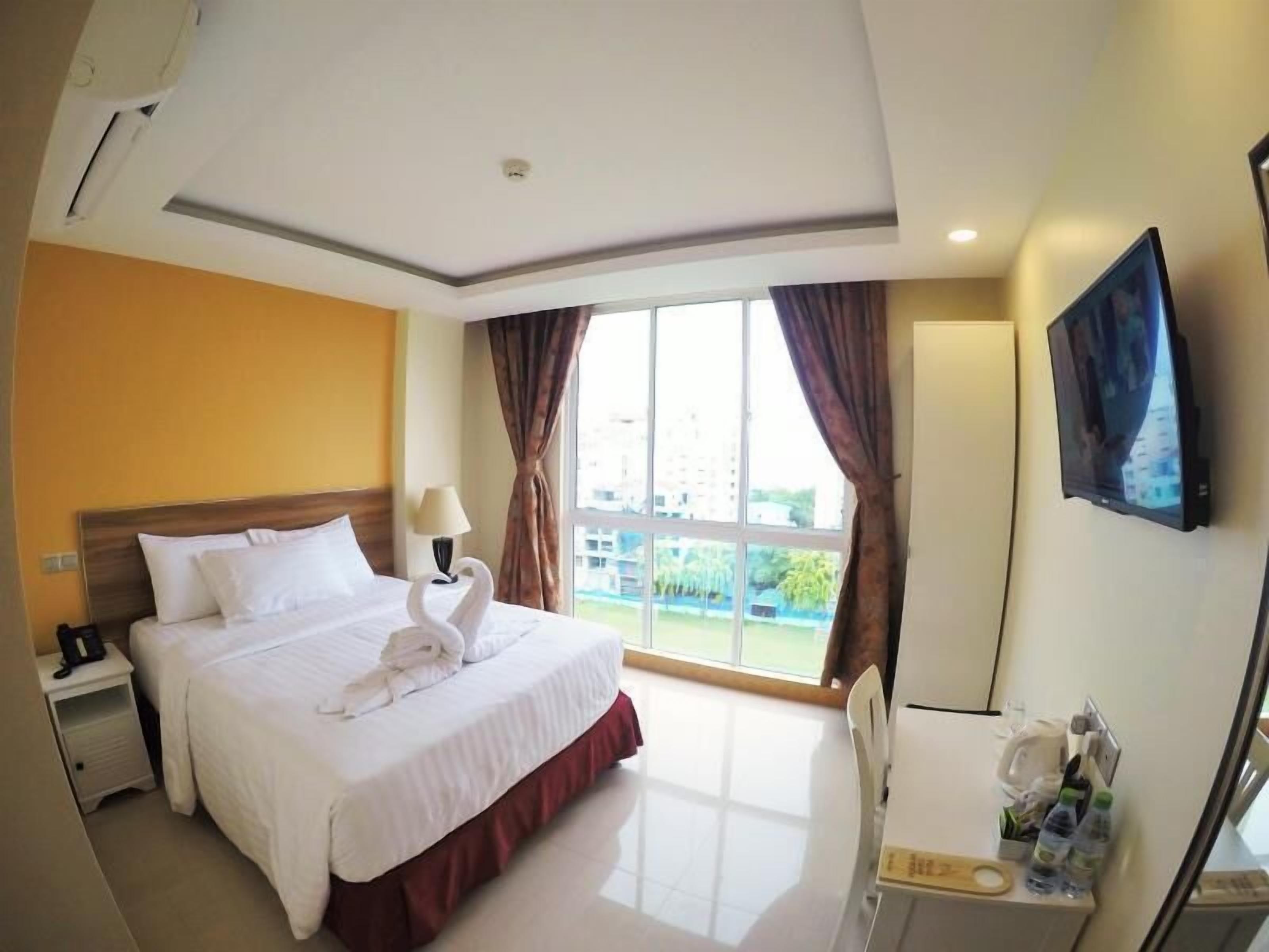 A hotel room with a bed, a desk, a chair, a TV, and a window with curtains.